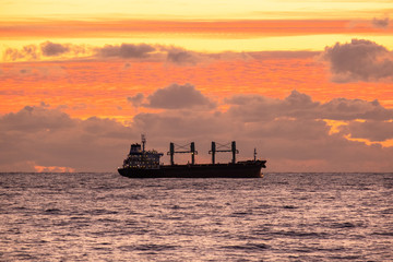Sunset over the sea. A naval ship on the horizon. Oil tanker ship at sea on a background of sunset sky