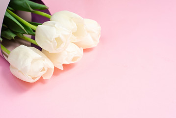 Fototapeta premium Bouquet of white tulips wrappen in pink paper. Minimal nature flat lay. Greeting card for Mother's Day and March 8th. Tender concept of spring holidays