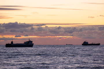 Orange sunset over the sea. Industrial ship on the roadstead. Beautiful clouds in the sky. Cargo transportation by sea. Marine