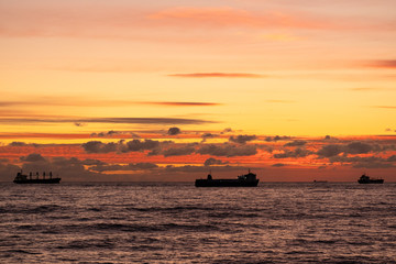 Naklejka na ściany i meble Orange sunset over the sea. Industrial ship on the roadstead. Beautiful clouds in the sky. Cargo transportation by sea. Marine