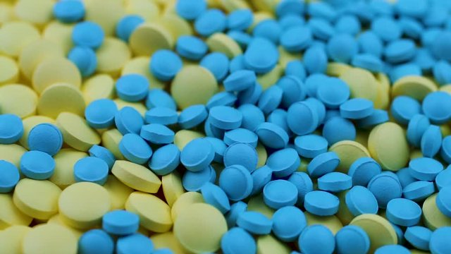 Blue pills fall on yellow ones on top and rotate on a table in a pharmacy