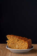 Top view of portion of carrot cake, in blue and white plate on wooden table with black background, in vertical, with copy space