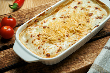 Appetizing Italian lasagna in a special baking dish. Homemade lasagna with melted cheese and various fillings (vegetables, meat) on a wooden background