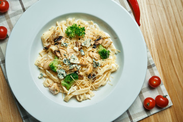 Appetizing, homemade pasta (tagliatelle) with broccoli, blue cheese and chicken in a white plate on a wooden background. Traditional italian cuisine