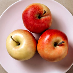 three red-green apples on a pink plate