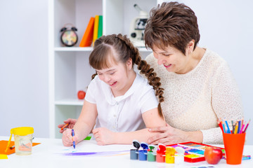 Fototapeta premium Girl with Down Syndrome engaged in creativity with her mother at home at the table
