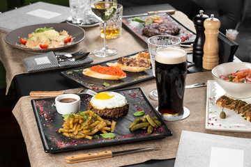Fried minced beef steak with egg, fried potatoes and glass of dark beer on the table at restaurant