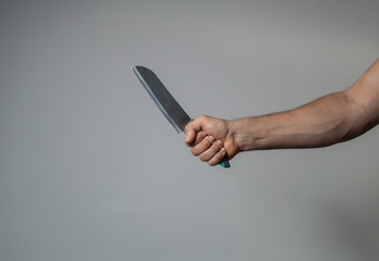 Male hand holds a big sharp knife on a gray wall background
