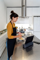 Brunette woman cooking a recipe from a digital tablet in a modern kitchen