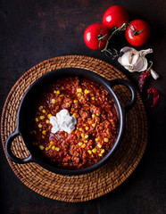 Chili con Carne in a black iron bowl on a dark dish decorated with tomatoes, flatlayphotography