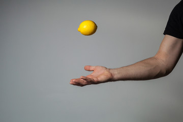 A man's hand throws a whole lemon into the air against a gray wall background