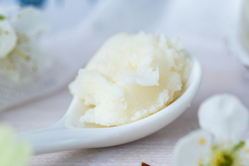 Shea butter on a white ceramic spoon on a white table in spring time. Karite cream for skin care. Raw home made butter for skin care.
