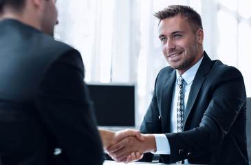 handshake of business partners sitting at a Desk