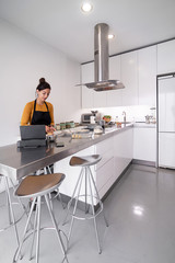 Brunette woman cooking a recipe from a digital tablet in a modern kitchen