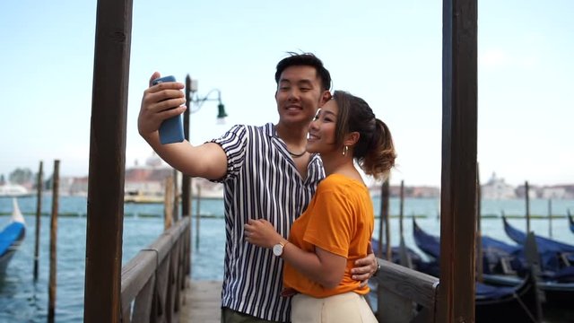 Asian couple in love take a selfie in Venice near the gondolas and they are embraced