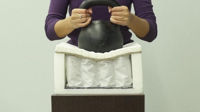 Woman hands puts a heavy weight on an orthopedic foam mattress