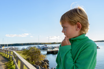 Fototapeta na wymiar Profile view of young handsome boy at wooden pier near the river