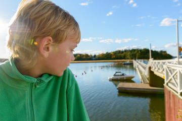 Fototapeta premium Profile view of young handsome boy looking at view of wooden pier near the river