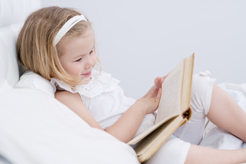 Little girl reading a book in her room in the bedroom. Home education concept.