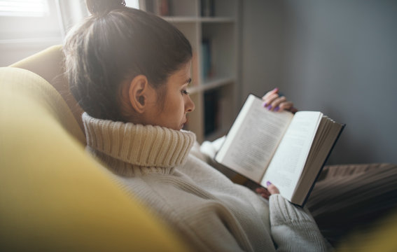 Close up of pretty girl in sweater reading favorite book