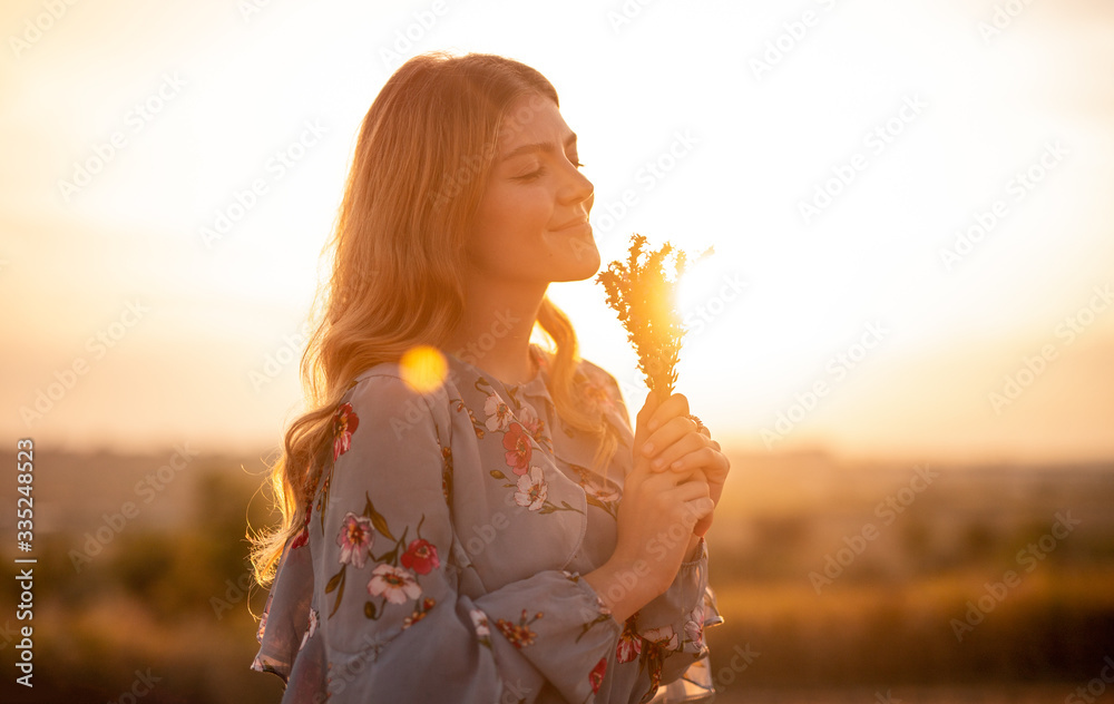 Wall mural Happy woman with flowers enjoying sunset in field