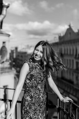 Young girl in a floral dress stands on a city balcony