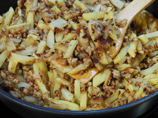 Background delicious fried potatoes with minced meat on a wooden spoon in a pan closeup. A simple rustic dish of French fries with meat.