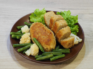 Fried fish cutlets, chicken cutlets, turkey cutlets, green string beans, cauliflower, lettuce leaves  on a light wooden background, closeup. Delicious meat diet dish with vegetables, top view