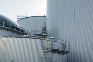 Naklejka premium part of the metal industrial tanks outdoor. roof of technological building at the industrial plant on background. Equipment and appliances at the gas company. metal ladder stairs on the tank