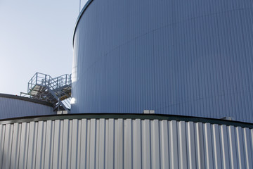 Obraz premium part of the metal industrial tanks outdoor. roof of technological building at the industrial plant on background. Equipment and appliances at the gas company. metal ladder stairs on the tank
