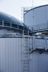 part of the metal industrial tanks outdoor. roof of technological building at the industrial plant on background. Equipment and appliances at the gas company. metal ladder stairs on the tank