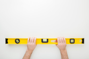 Man hands holding yellow spirit level on light gray table background. Building tool for floor, wall, ceiling or other surfaces level precision. Point of view shot. Empty place for text. Top down view.