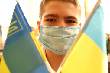 A young boy in a protective mask holds the national flags of Ukraine yellow-blue. Stop coronavirus....