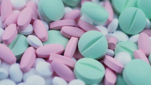 Round green pills fall on white vitamins and pink oval antibiotics. Closeup