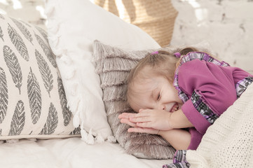 little smiling three year old girl is lying on the bed and trying to sleep
