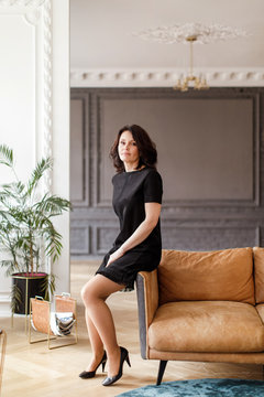 Woman in a black dress sits on the back of a sofa in the interior