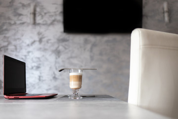 Latte macchiato w kubku na stole w biurze obok laptopa.