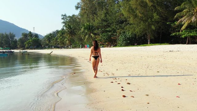 Attractive young woman enjoying walk on seaside, barefoot on white sandy beach washed by calm clear sea water in Jamaica