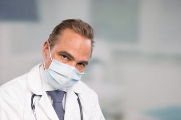 exhausted male doctor in lab coat and tie in front of a clinic room