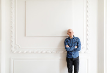 Portrait of a bald brutal Man in jeans standing against a white wall