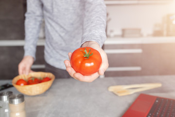 Fototapeta Mężczyzna pokazuje z bliska pomidor który trzyma w dłoni w kuchni. obraz