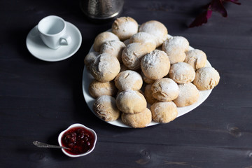 baked honey-cakes with sugar powder on white plate on black background with raspberry jam, cup for coffee 