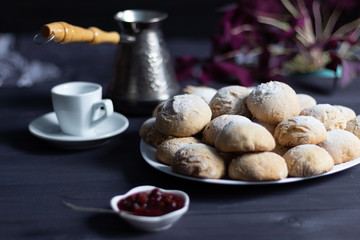 baked honey-cakes with sugar powder on white plate on black background with raspberry jam and coffee