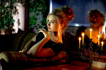 A beautiful, young blonde with a fashionable hairstyle and model appearance, sitting in a restaurant against the background of a mirror by candlelight.