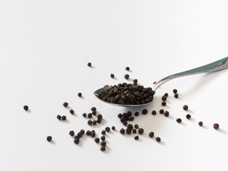Fototapeta na wymiar black peppercorns on metal spoon in white background 