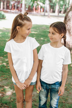 Two little girls in white t-shirts standing in park outdoor. Mock up.