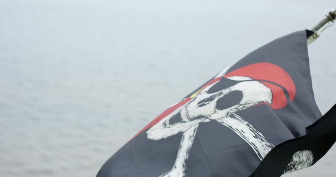 Pirate flag flapping in wind on ocean - close up - slow motion