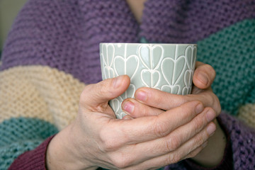 Close-up of hand holding coffee cup, purple and teal colours