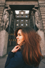 Obraz premium Portrait of a girl with long hair in a jacket against the background of an old historical building in St. Petersburg, an architectural monument with sculptures and columns
