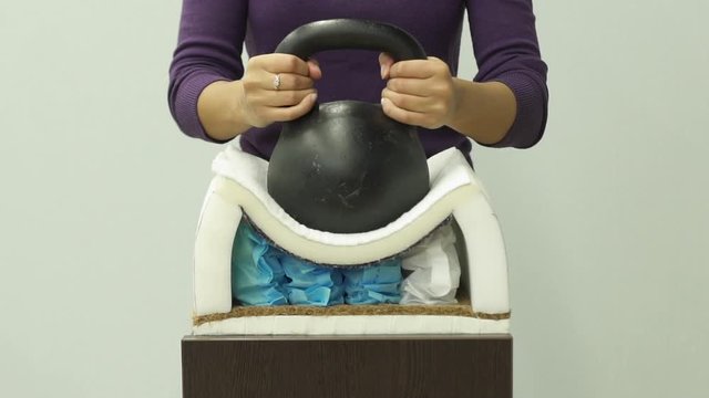 Woman hands puts a heavy weight on an orthopedic foam mattress with spring